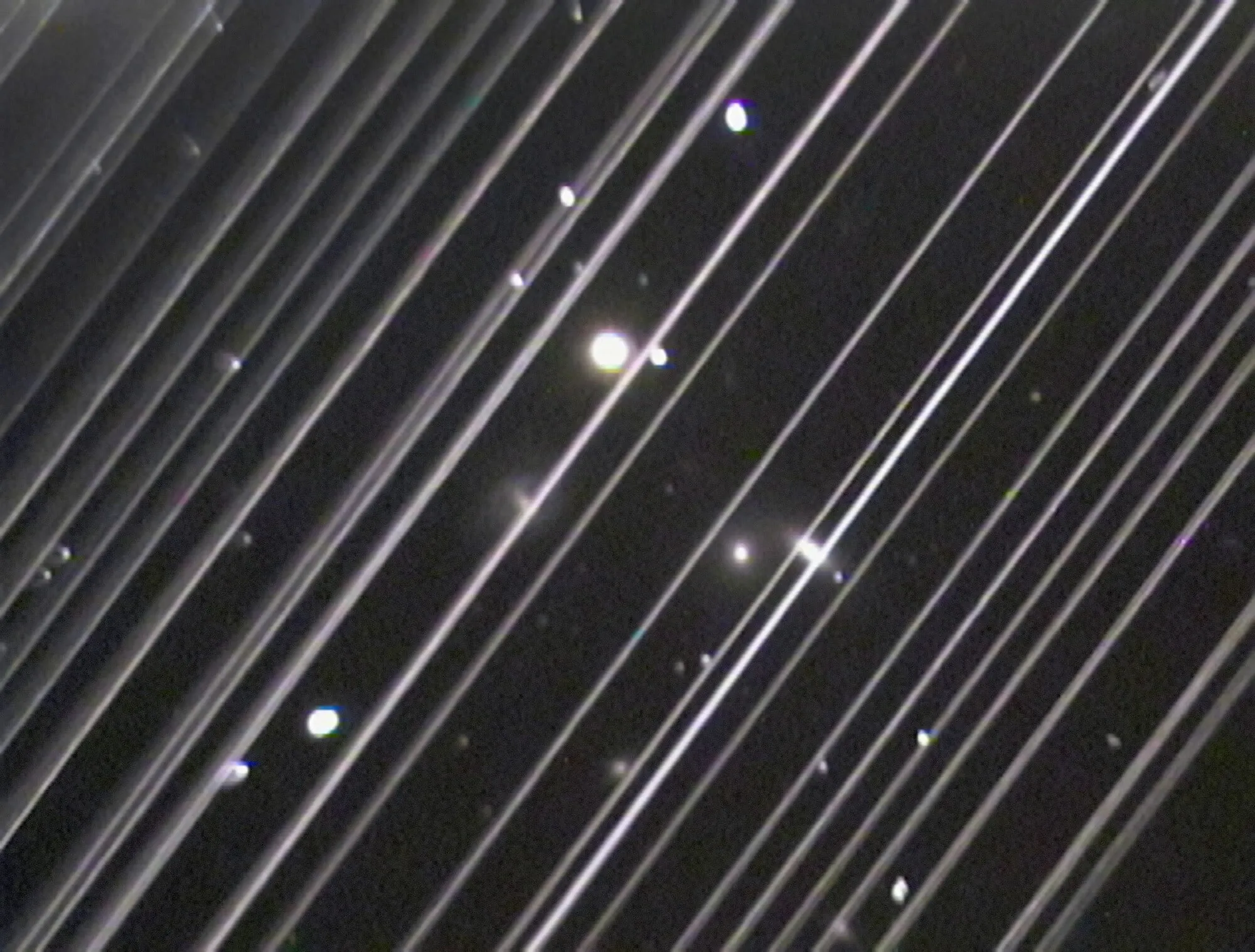 Dozens of bright parallel streaks crossing a telescope image of a star field.